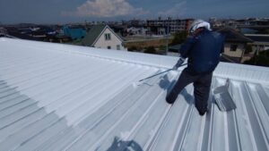 遮熱塗料を塗布中の職人の手元｜鈴鹿市 倉庫屋根塗装の中塗り工程｜ペイントホームズ鈴鹿店